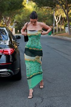 a woman in a green dress walking down the street with her hand on her hip