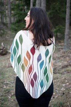 a woman standing in the woods wearing a colorful knitted shawl