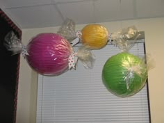 three colorful balls hanging from the ceiling in front of a window with ribbons on them