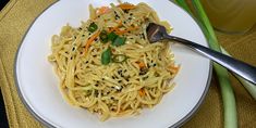 a white plate topped with noodles and carrots next to a glass of orange juice