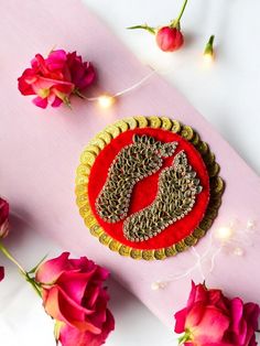 a red and gold brooch sitting on top of a pink surface next to flowers