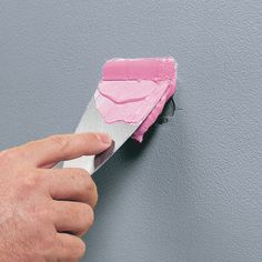 a hand is holding a paint roller and painting the wall with pink paste on it