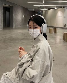 a woman with headphones and a face mask sits in an empty room while looking at the camera