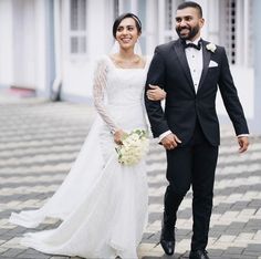 a bride and groom are walking down the street in their wedding attire, dressed in black tuxedos