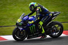 a man riding on the back of a blue motorcycle down a race track with grass in the background