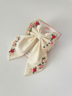 a white bow with pink flowers and pearls on the side, sitting on top of a card