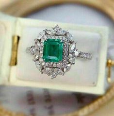 an emerald and diamond ring sits in a white box with gold trimmings on it