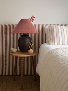 a small table with a lamp on it next to a striped wallpapered headboard