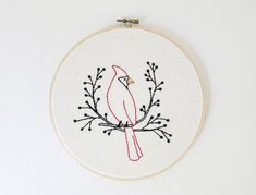 a red bird sitting on top of a tree branch embroideryed in white hoop with black thread