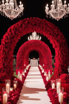 a long aisle with red roses and candles in the center is lit by chandeliers