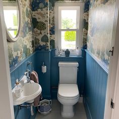 a small bathroom with blue walls and floral wallpaper, along with a white toilet