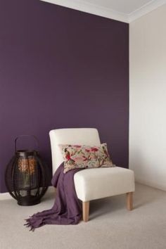 a white chair sitting next to a purple wall in a room with a lamp on the floor