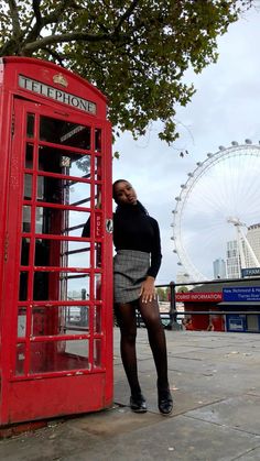 a woman standing next to a red phone booth