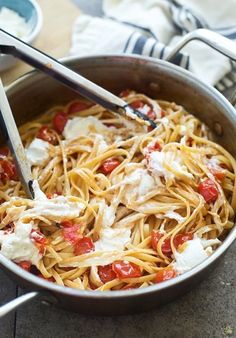 a pot filled with pasta and sauce on top of a wooden table next to a fork