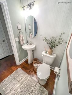 a white toilet sitting next to a sink in a bathroom on top of a hard wood floor