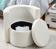 a white bed with a round storage container on the floor in front of it,