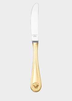 a knife that is sitting on top of a table with gold trimmings and a white handle