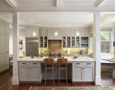 a large kitchen with white cabinets and wooden flooring, along with two bar stools