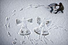 two people are standing in the snow with their handprints on them and one person is kneeling down