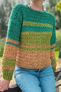 a woman sitting on top of a wooden bench wearing a green and yellow crochet sweater