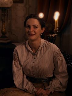 a woman sitting on top of a chair in a room next to two lit candles