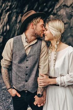 a man and woman standing next to each other in front of a rock wall holding hands