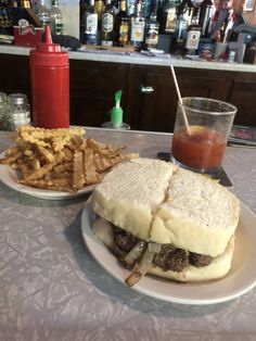 a plate with a sandwich and some fries on it next to a drink at a bar