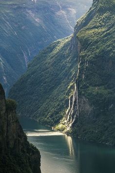 the mountains are covered in green vegetation and there is a boat on the water below