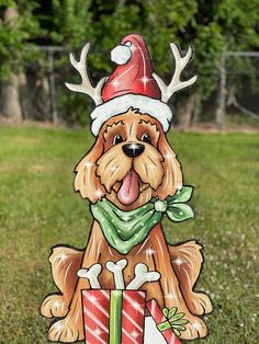 a brown dog wearing a santa hat and green scarf sitting next to a christmas present