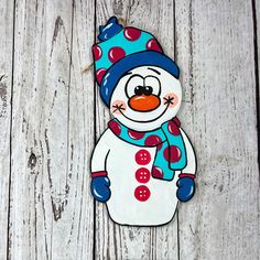 a snowman ornament is hanging on a white wooden wall with a blue hat and scarf