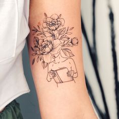 a woman's arm with flowers on it and a book in the other hand