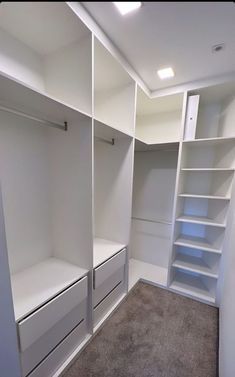 an empty walk in closet with white shelving and gray carpeted flooring on the walls