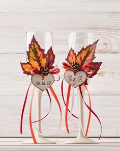 two wine glasses decorated with fall leaves and ribbons are sitting next to each other on a table