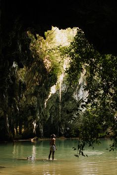 a man standing in the middle of a river surrounded by trees and rocks, with his back turned to the camera