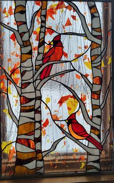 a stained glass window with a red bird perched on a tree in front of it