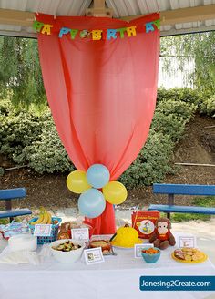 an outdoor birthday party with balloons, cake and snacks on a table in front of a canopy