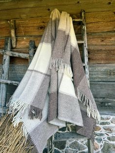 two gray and white blankets hanging on a wooden ladder next to a stone wall with logs