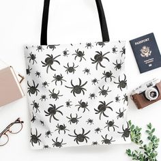 a black and white spider print tote bag next to an open passport, camera, sunglasses, and other items