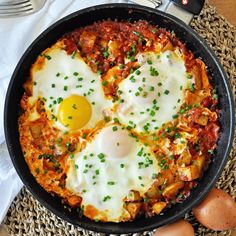 two fried eggs are in a skillet on a table with utensils and silverware