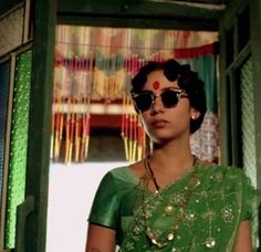 a woman in a green sari is standing by an open door and looking at the camera