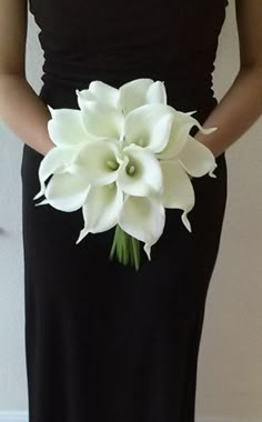 a woman in a black dress holding a bouquet of white calla lilies on her wedding day