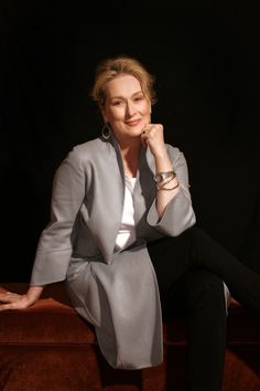 a woman sitting on top of a brown couch next to a black wall with her hand under her chin