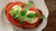 a sandwich with tomatoes, mozzarella and lettuce sits on a white plate