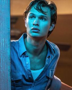 a young man leaning against a wooden pole looking at the camera with an intense look on his face