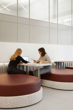 two women sitting at a table in an office setting with circular seating and round tables