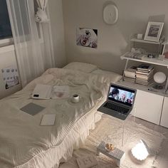 a laptop computer sitting on top of a bed next to a book shelf and window