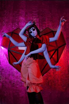 a woman dressed in costume and makeup holding an umbrella with her arms spread out to the side