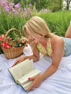 a woman laying on the ground reading a book with flowers in the backgroud