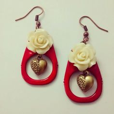 two pairs of red and gold earrings with white flowers on them, hanging from hooks