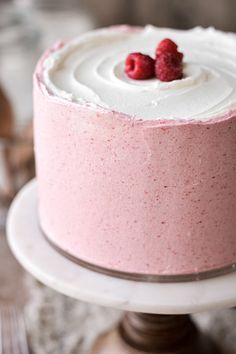 a pink cake with white frosting and two raspberries on top, sitting on a plate